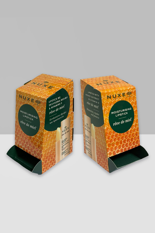 Two boxes of Nuxe moisturising lipstick. The boxes are orange and green with a honey comb pattern and a photo of the Nuxe lipstick.