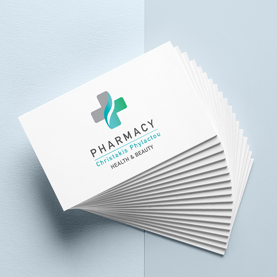 spread out stack of business cards set on a light blue background. White business cards with pharmacy cross logo in teal and green. with teal and black text.